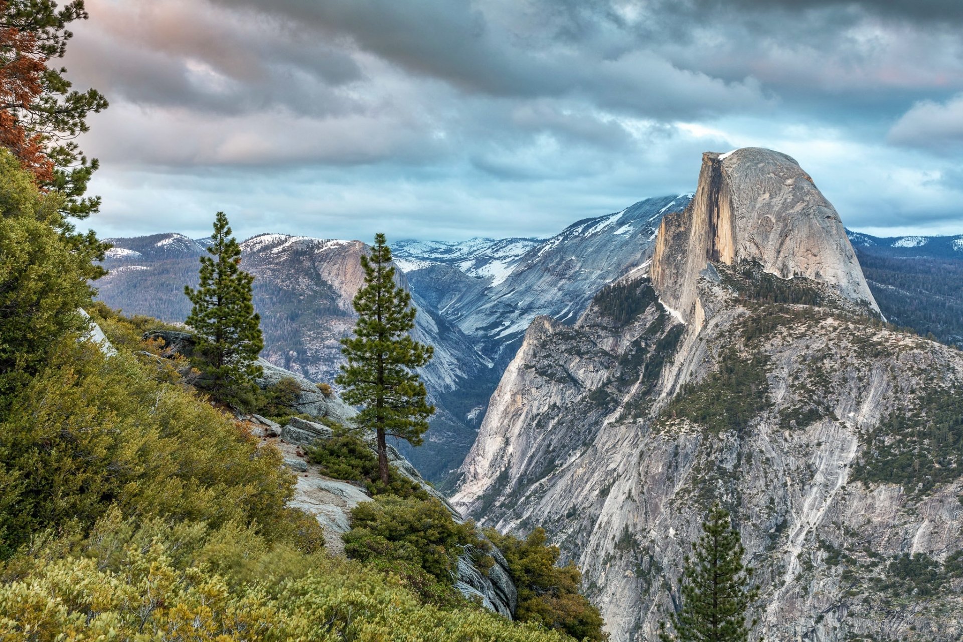 HD desktop wallpaper showcasing the iconic Half Dome and surrounding granite cliffs in Yosemite National Park under a vibrant sky with lush greenery in the foreground.