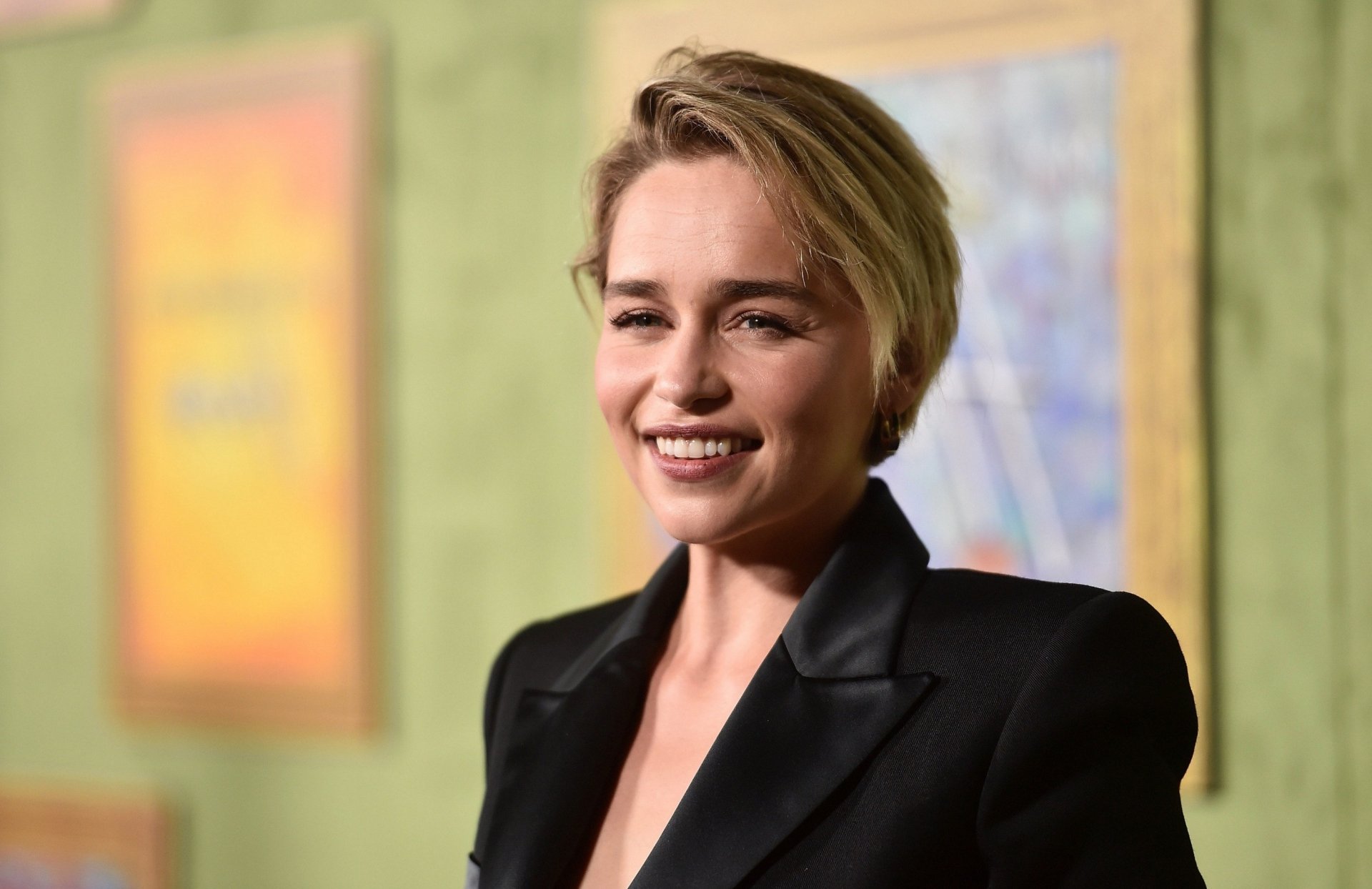 Short-haired smiling woman in a black blazer, head-and-shoulders portrait against a soft green backdrop — 2K Quad HD PC desktop wallpaper/background.