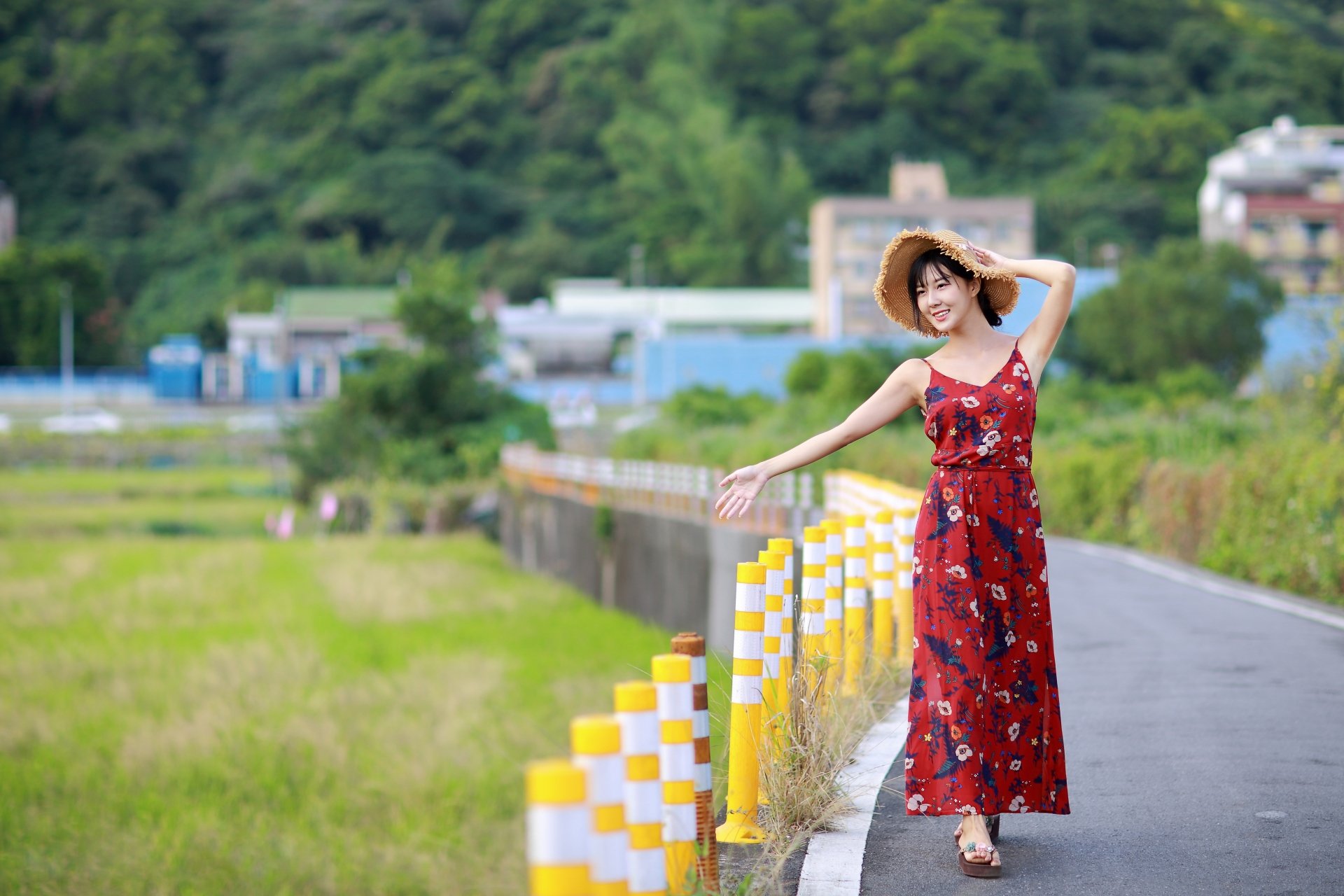 A woman in a red floral dress and wide-brimmed hat poses confidently on a rural road, captured in vibrant 4K Ultra HD quality.