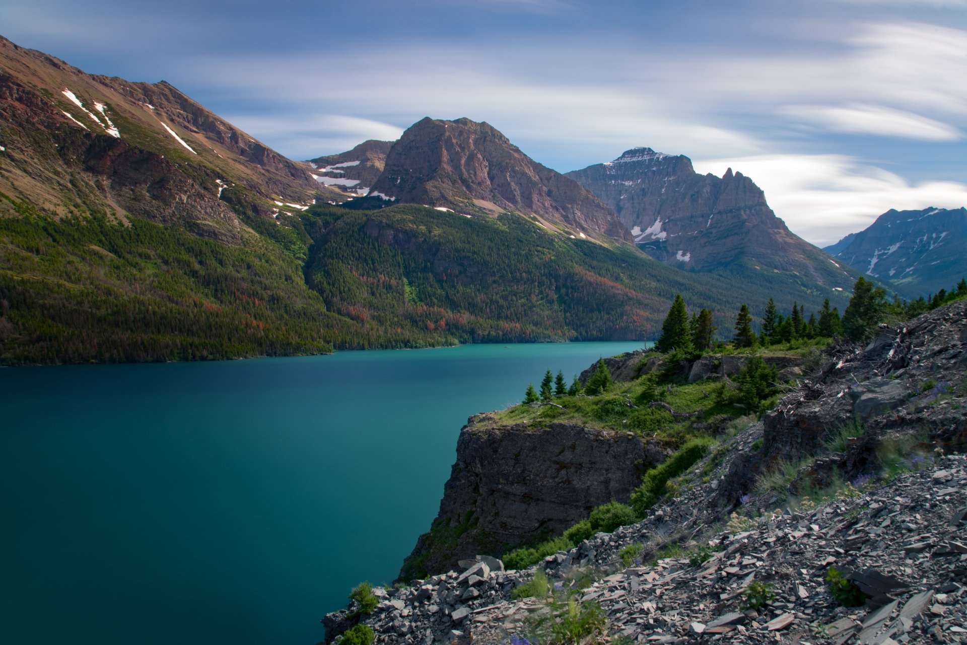 A stunning 4K Ultra HD view of a serene lake surrounded by majestic mountains in Glacier National Park, showcasing pristine nature and vivid colors.