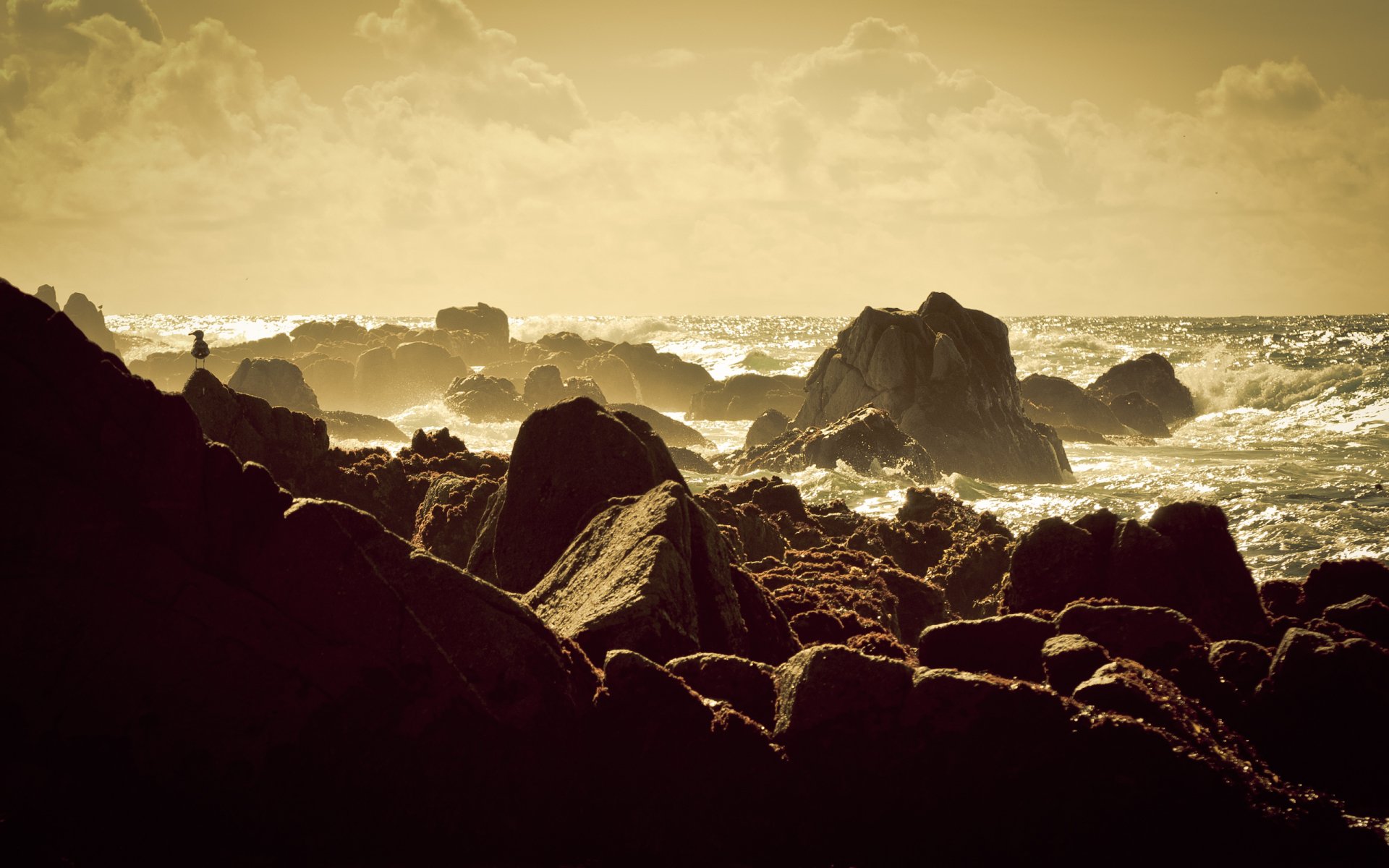 HD PC desktop wallpaper capturing a serene beach scene with rugged rocks and gentle waves under a golden sky.