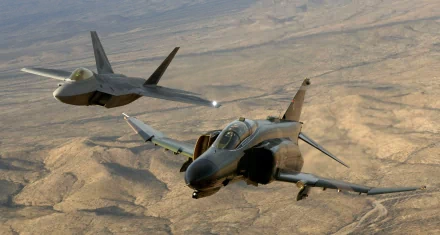 A high-definition desktop wallpaper featuring an aerial view of a McDonnell Douglas F-4 Phantom II and a Lockheed Martin F-22 Raptor in flight over a desert landscape, showcasing their military jet fighter prowess.