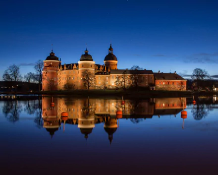 Gripsholm Castle in Mariefred, Sweden, illuminated at dusk, reflected beautifully in the calm water, showcasing the historic man-made fortress.