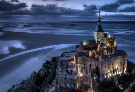 A stunning 4K Ultra HD image of the illuminated Mont Saint-Michel, a religious landmark, set against a dramatic twilight sky and expansive tidal flats.