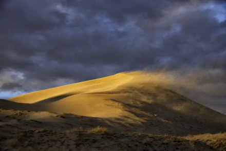 Sunlit sand dune shaped by wind under dramatic cloud-filled sky in a desert, captured in stunning 4K Ultra HD for a PC desktop wallpaper.