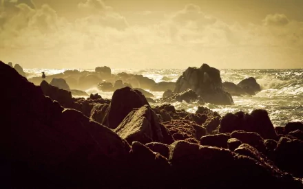 HD PC desktop wallpaper capturing a serene beach scene with rugged rocks and gentle waves under a golden sky.