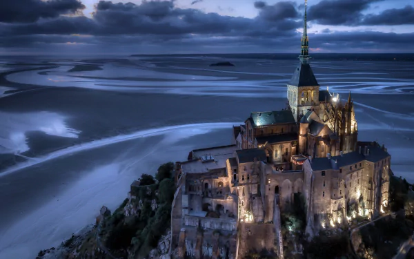 A stunning 4K Ultra HD image of the illuminated Mont Saint-Michel, a religious landmark, set against a dramatic twilight sky and expansive tidal flats.