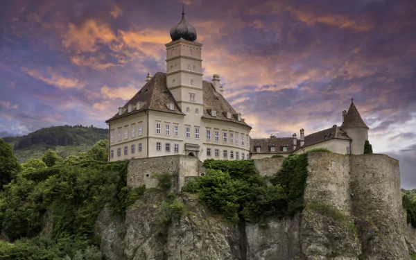 Schloss Schönbühel, a historic man-made castle perched on a cliff in Hungary, captured in stunning 4K Ultra HD against a dramatic sunset sky.
