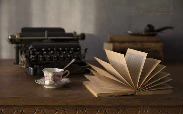 A vintage typewriter, open book, stacked old books, and a floral teacup on an ornate wooden table, captured in 4K Ultra HD as a PC desktop wallpaper.