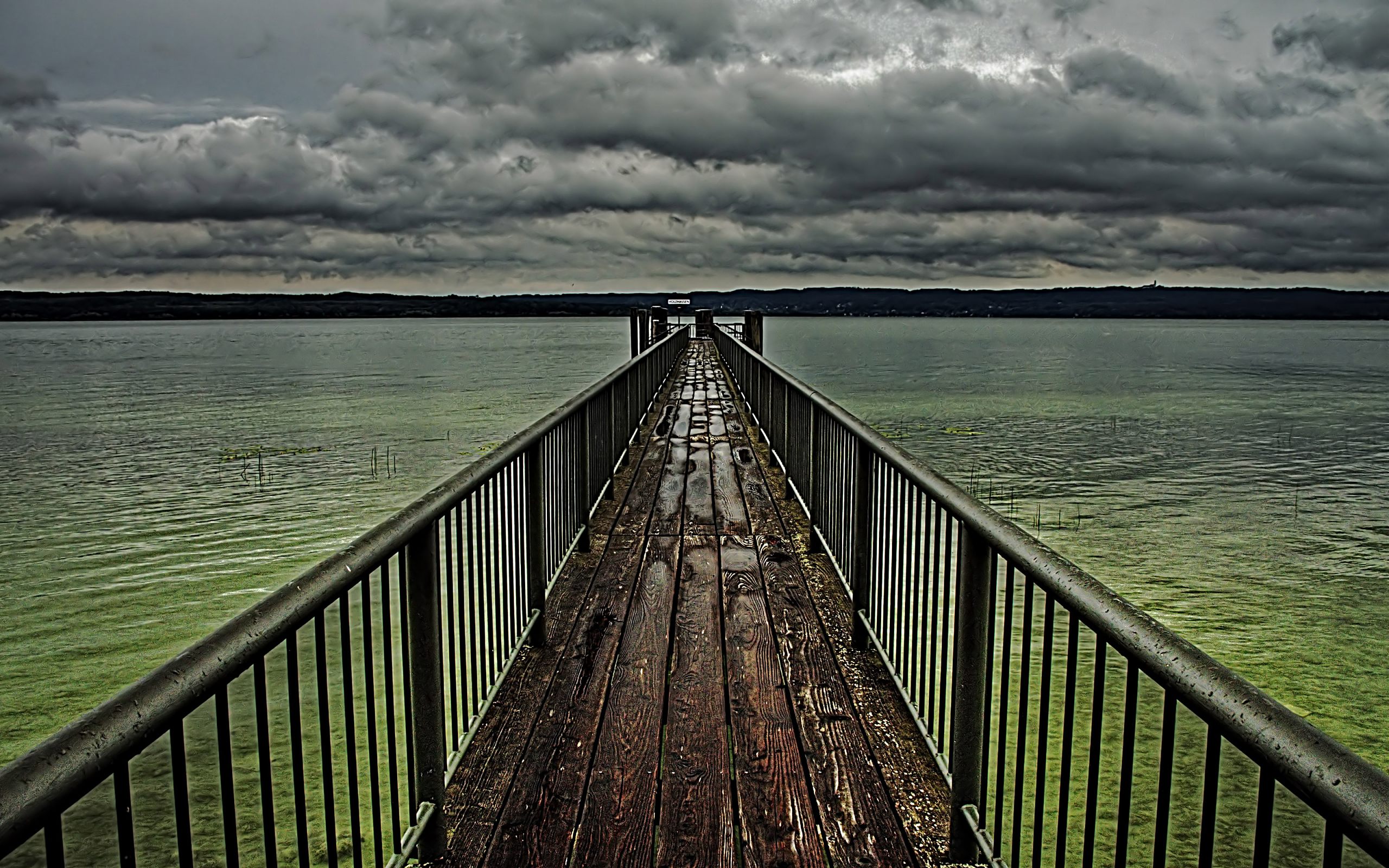 Wooden pier stretching into a stormy sky, named nachabzugdesgewitters.