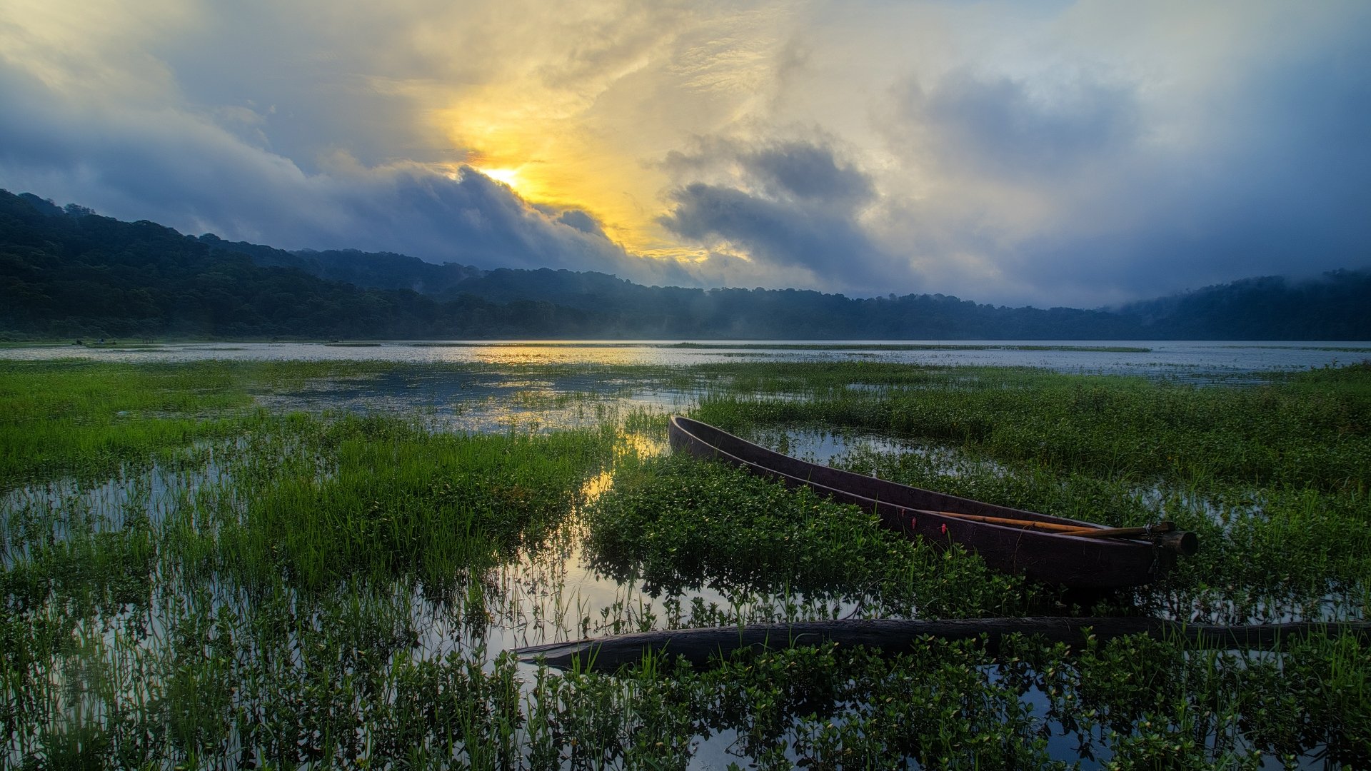 A serene 4K Ultra HD desktop wallpaper featuring a boat on a lake surrounded by lush vegetation under a dramatic cloudy sky at sunrise or sunset.