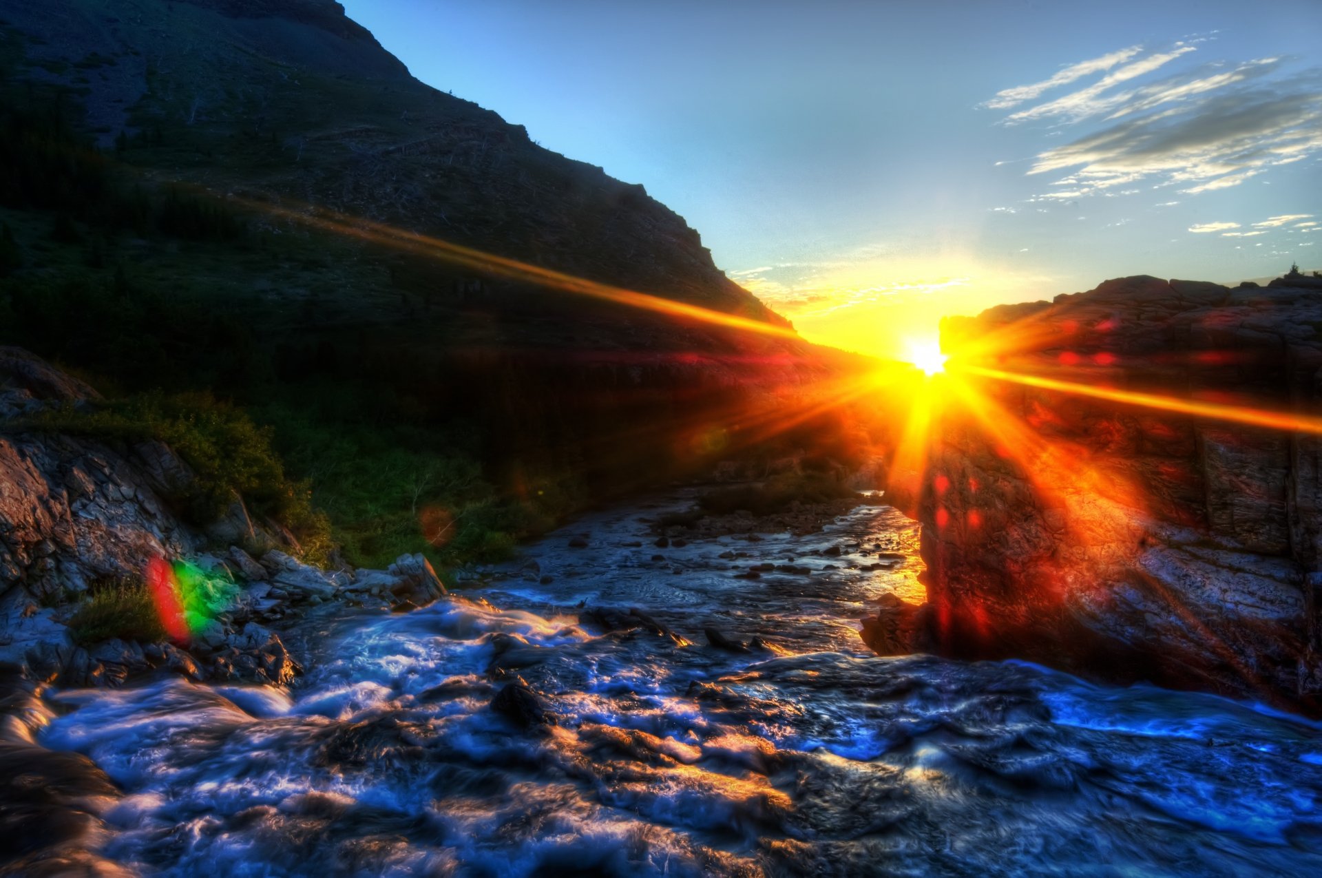 4K Ultra HD nature wallpaper capturing a vibrant sunset over a flowing stream surrounded by rugged hills and a partly cloudy sky.