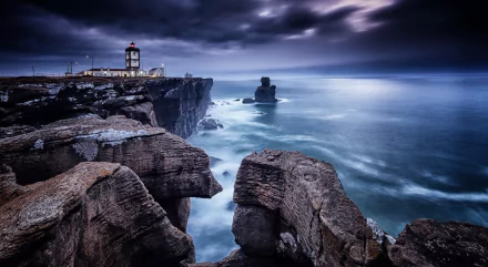 HD desktop wallpaper showing a dramatic seascape in Portugal with rugged cliffs and a man-made lighthouse under a moody sky.