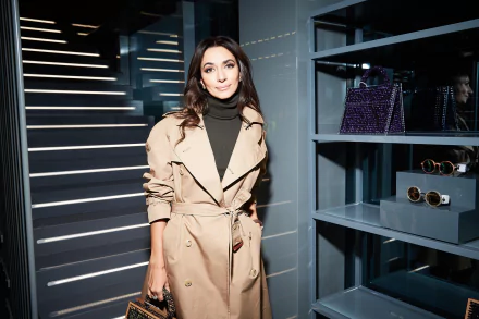HD desktop wallpaper featuring a woman with brown eyes and black hair wearing a beige coat, standing indoors near modern staircase and display shelves.
