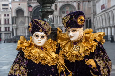 Two elaborately dressed figures in ornate Venetian costumes and masks pose during the Carnival of Venice, Italy, highlighting vibrant gold and purple colors in an HD desktop wallpaper.
