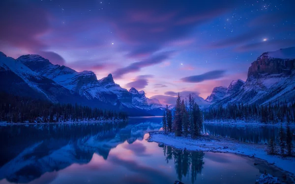 Winter night at Jasper National Park, Canada, featuring a serene lake reflecting snow-covered mountains under a vibrant twilight sky.