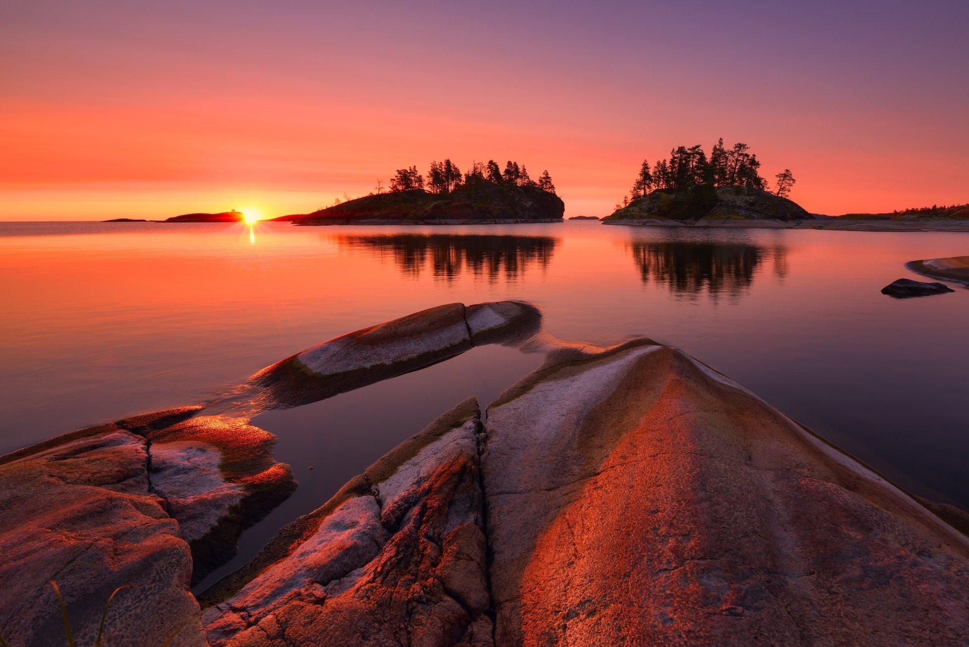 HD PC desktop wallpaper featuring a serene sunrise over a calm lake with rocky foreground and small tree-covered islands, showcasing natural beauty and tranquility.