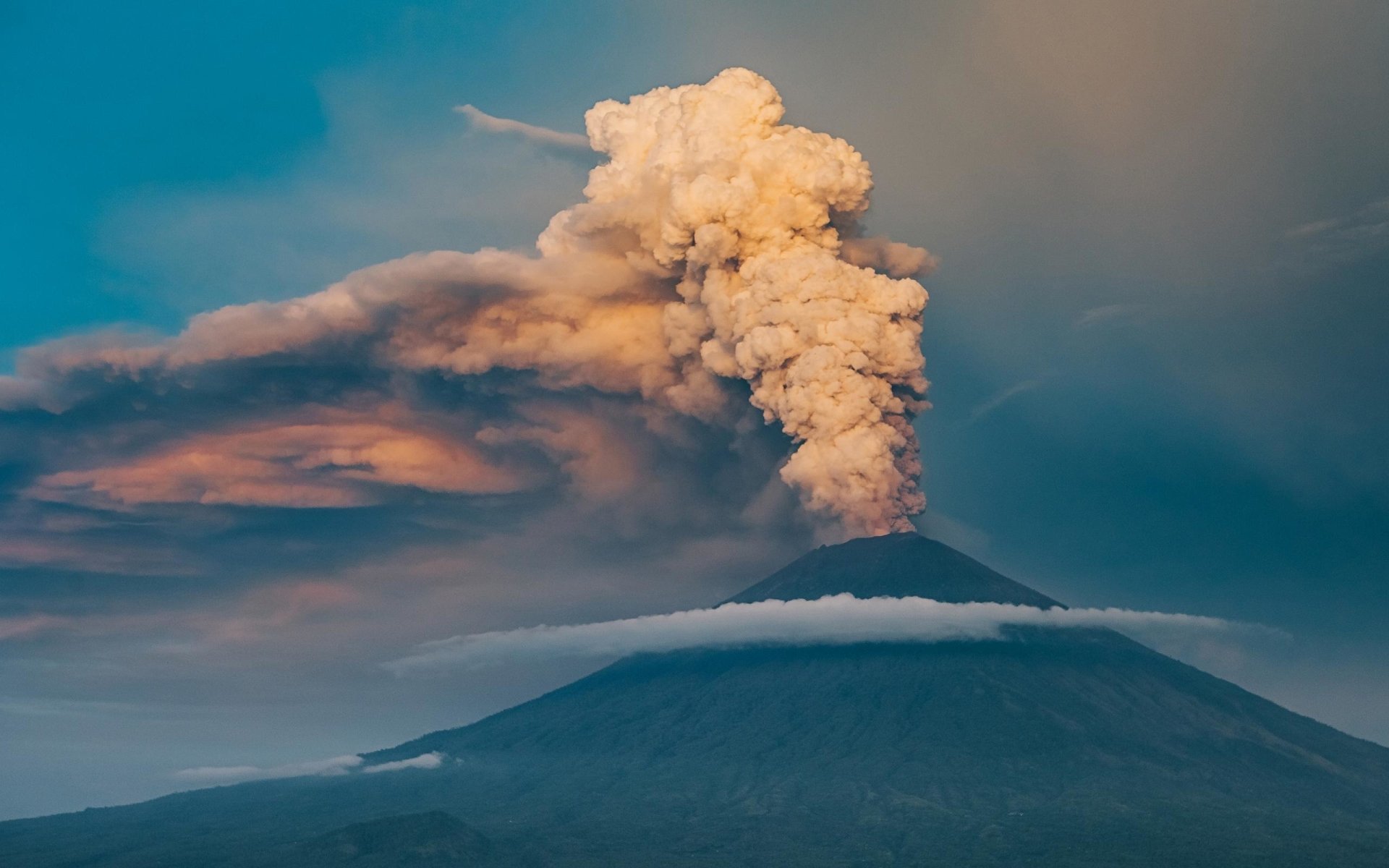HD desktop wallpaper of a volcanic mountain landscape with thick smoke and ash clouds rising against a vivid sky, showcasing the power of nature.