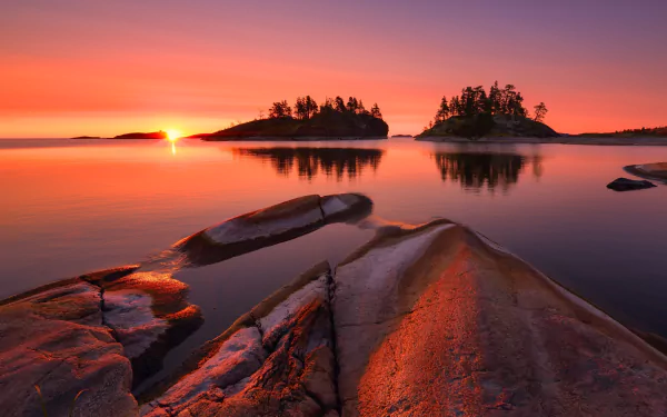HD PC desktop wallpaper featuring a serene sunrise over a calm lake with rocky foreground and small tree-covered islands, showcasing natural beauty and tranquility.