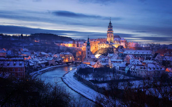 HD desktop wallpaper: winter night in the Czech Republic — illuminated historic city and castle above a snow-dusted river bend.