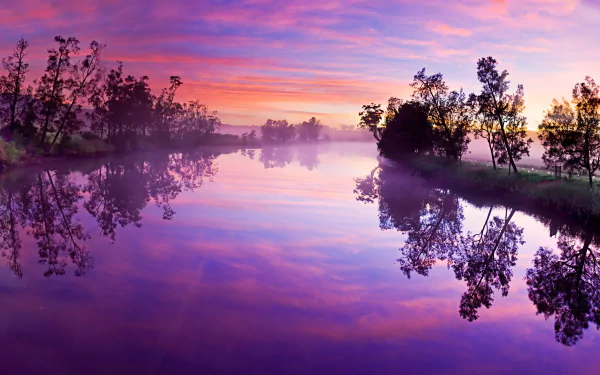 A serene 4K Ultra HD desktop wallpaper showcasing a calm river at dawn with vibrant clouds, fog, and nature reflected in the still water under a colorful sky.