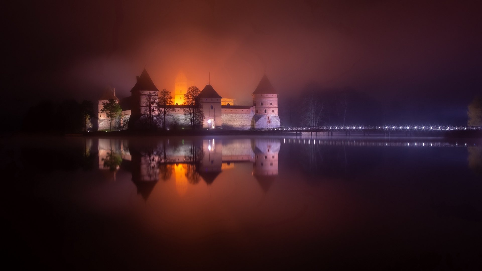 Trakai Island Castle at night in Lithuania, warm lights reflected on a calm lake; man-made medieval castle captured as a 4K Ultra HD PC desktop wallpaper background.
