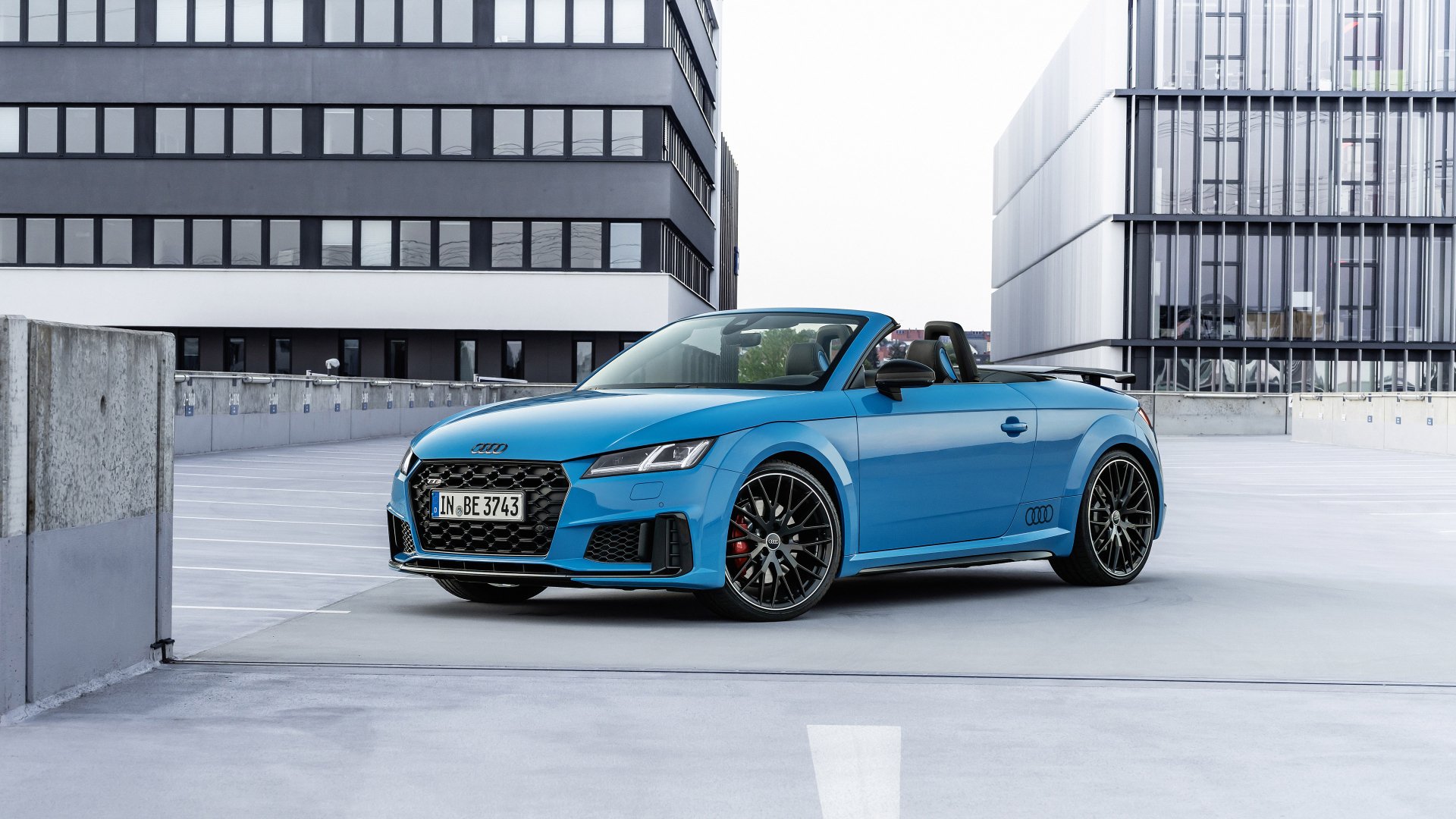 Blue Audi TTS Competition Plus cabriolet (Audi TT) parked on a rooftop between modern office buildings — 4K Ultra HD PC desktop wallpaper.