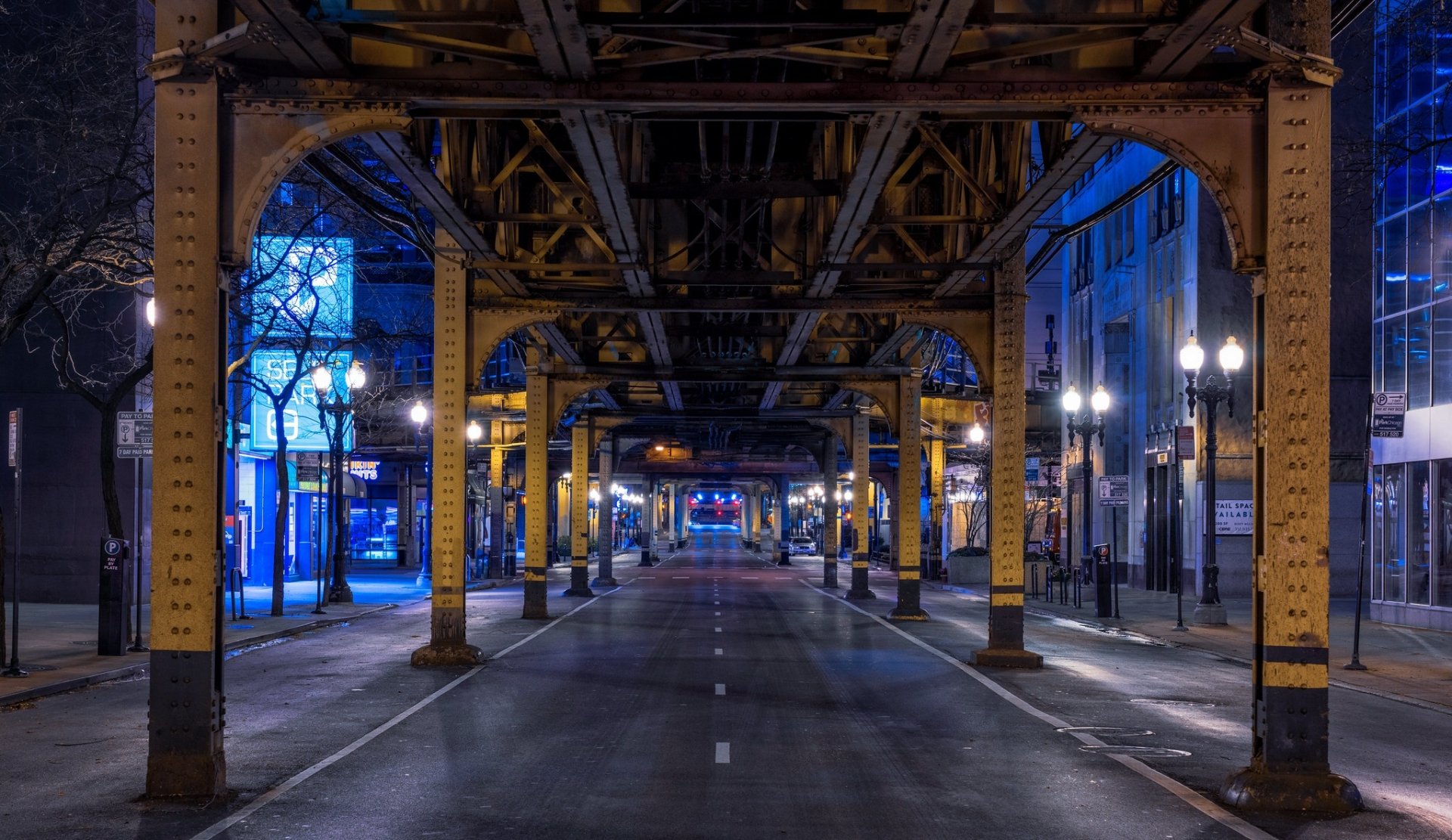 Nighttime view of an empty Chicago street under elevated train tracks, showcasing urban architecture in Illinois, captured in high-definition photography for a desktop wallpaper.