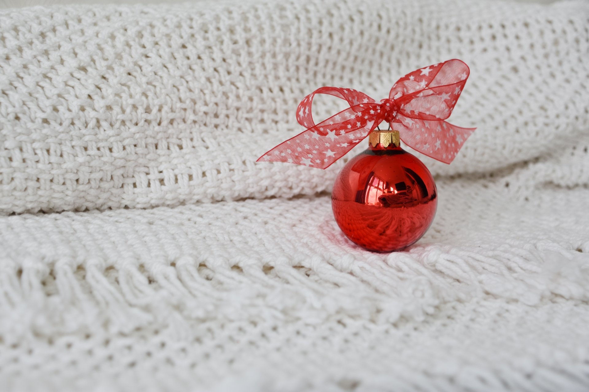 Red Christmas ornament with a sheer red bow resting on a white knitted blanket — festive holiday decoration; 5K Ultra HD PC desktop wallpaper/background.