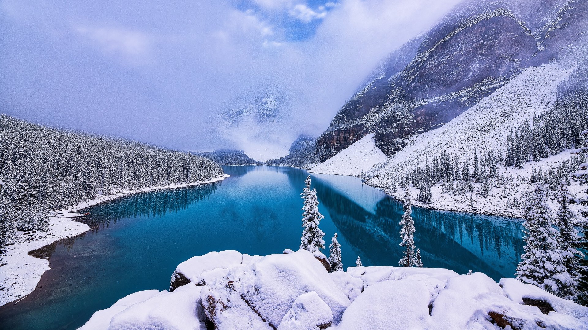 Snow-covered spruce trees and a tranquil lake set against snowy mountains in Alberta, Canada, captured in a stunning 4K Ultra HD winter landscape.