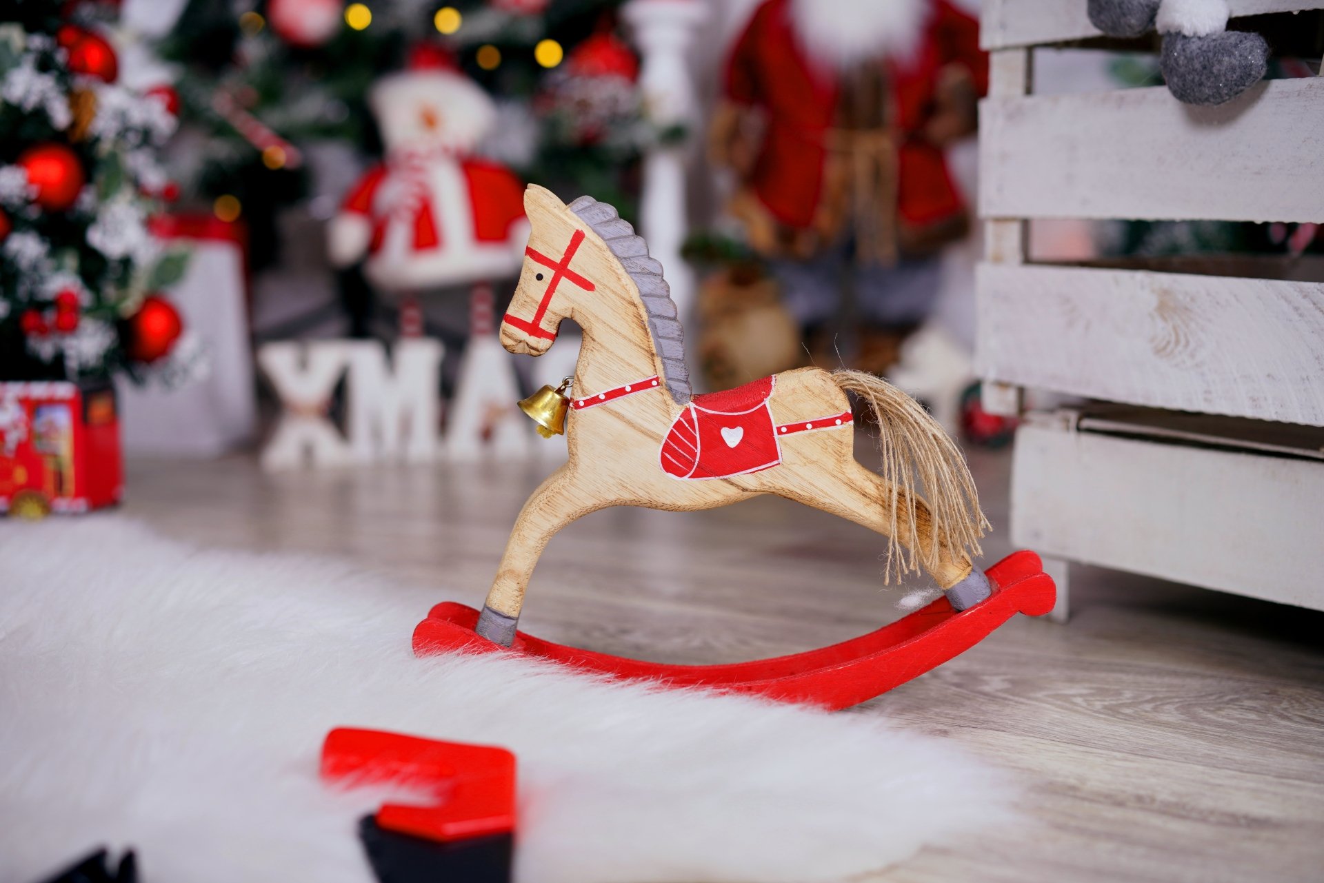 Wooden rocking horse toy ornament with red saddle among Christmas ornaments, tree and gifts in a festive holiday scene — 8K Ultra HD PC desktop wallpaper background.