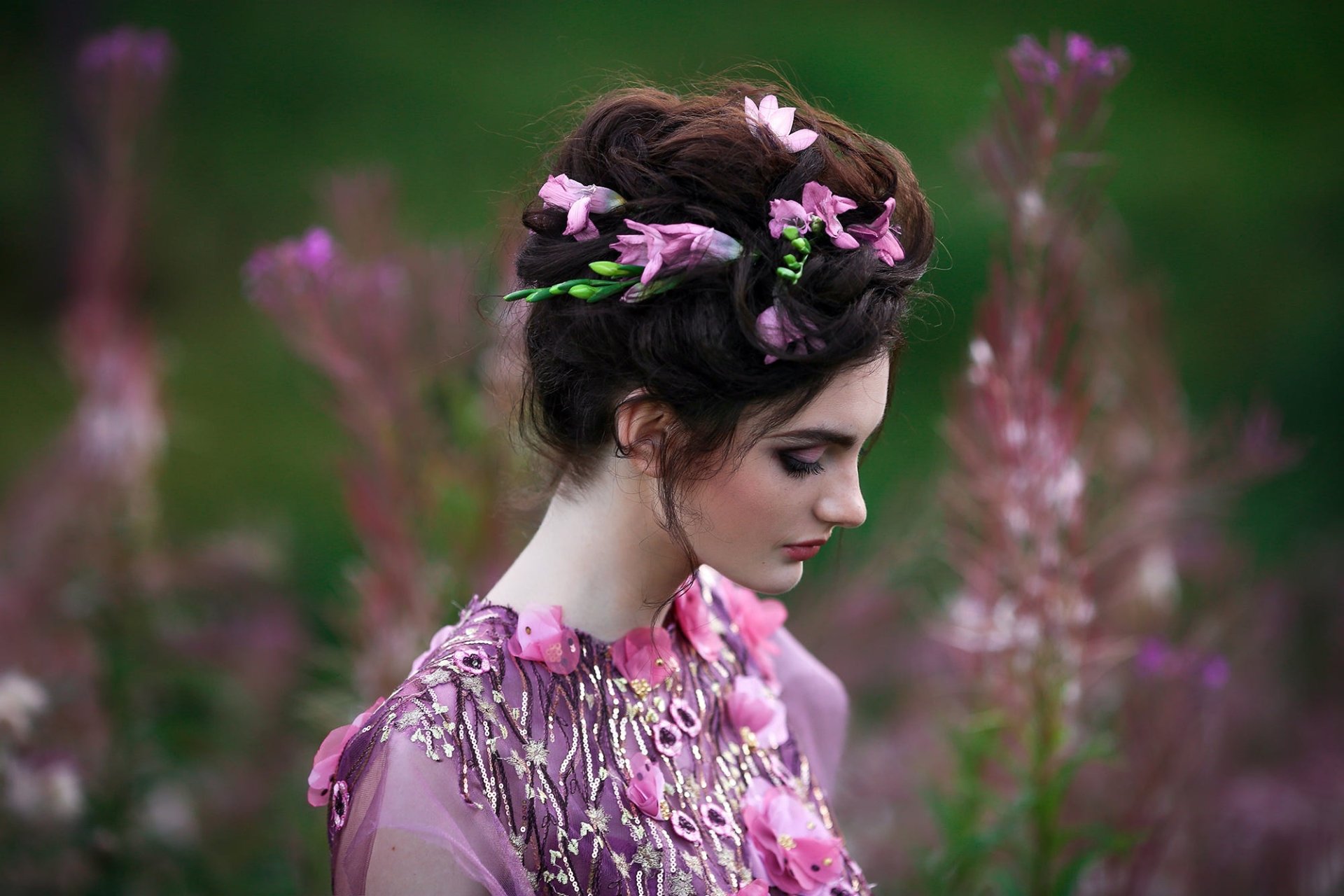 HD PC desktop wallpaper: profile portrait of a woman model—face in soft makeup, braided hair woven with pink flowers, conveying a dreamy mood against a blurred green floral background.