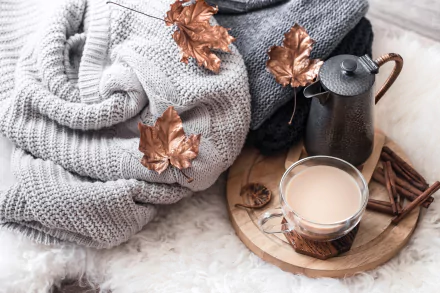 HD desktop wallpaper featuring a cozy still life scene of a cup of coffee on a wooden tray, surrounded by cinnamon sticks, an iron pot, a knit blanket, and copper-tinted leaves.