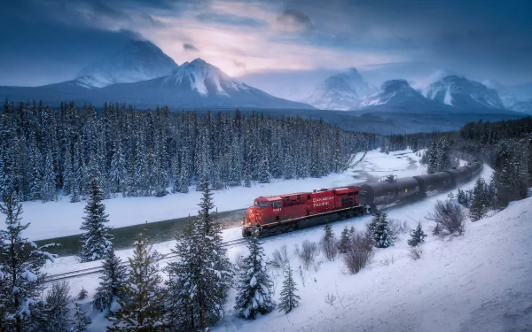 A red train moves through a snow-covered forest in Banff National Park, Canada, with snowy mountains in the background under a cloudy winter sky.