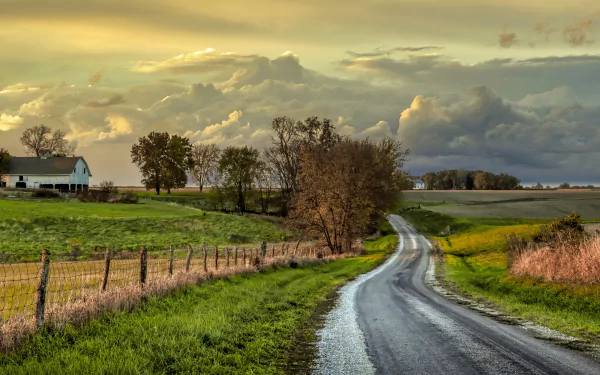 A winding farm road bordered by a wooden fence and grassy fields under a dramatic sky, captured in 4K Ultra HD for a PC desktop wallpaper.