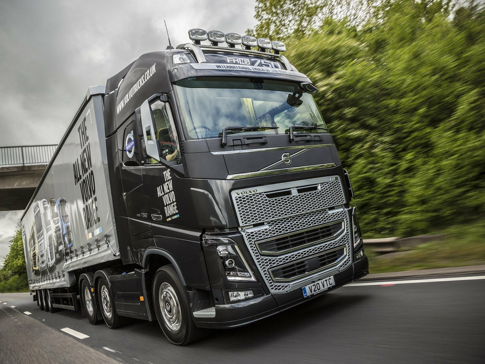 A striking HD desktop wallpaper featuring a Volvo FH16 750 truck in motion, showcasing its powerful design against a lush green backdrop.