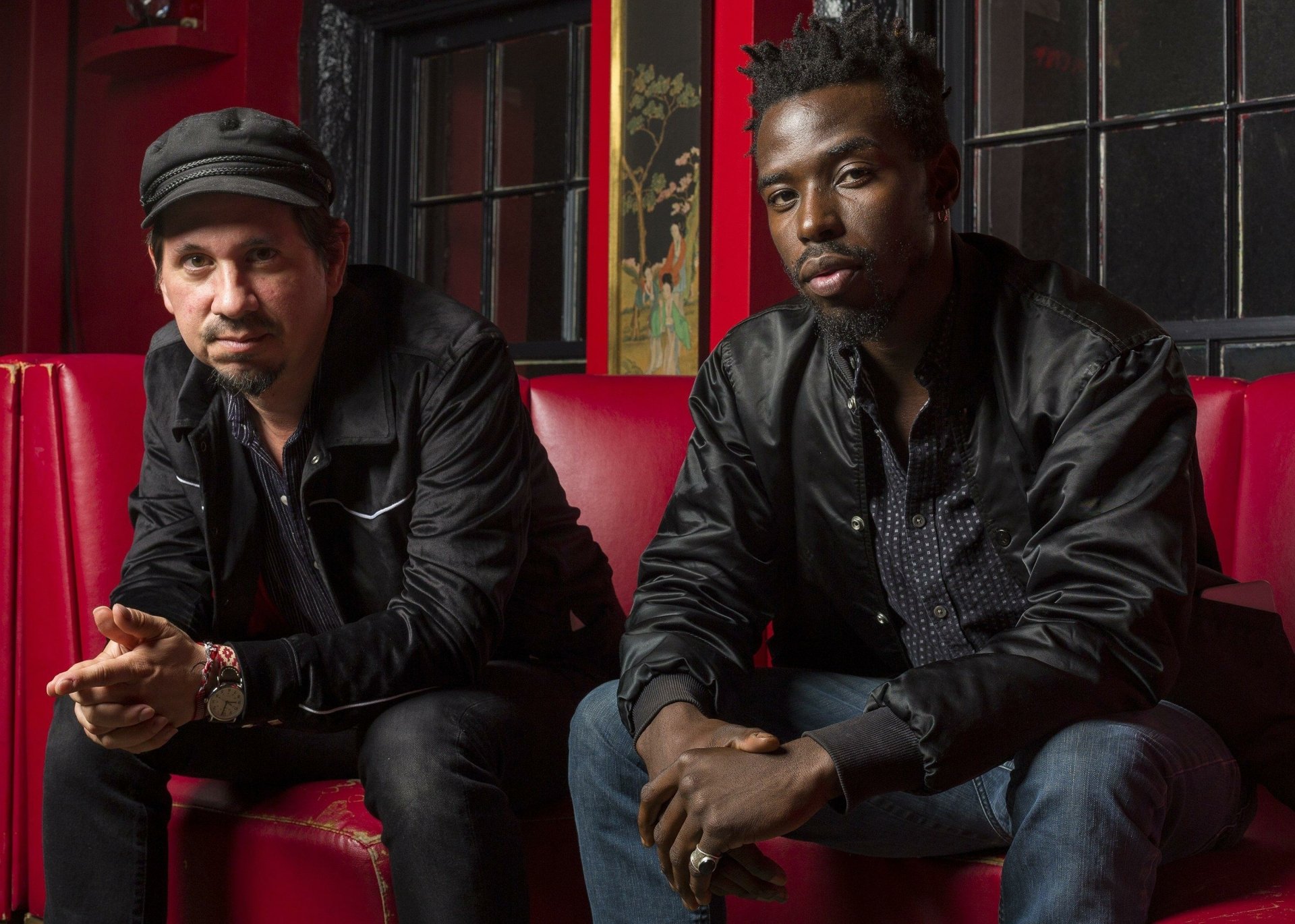 Two members of the music duo Black Pumas seated on a red couch, forming a stylish HD desktop wallpaper.