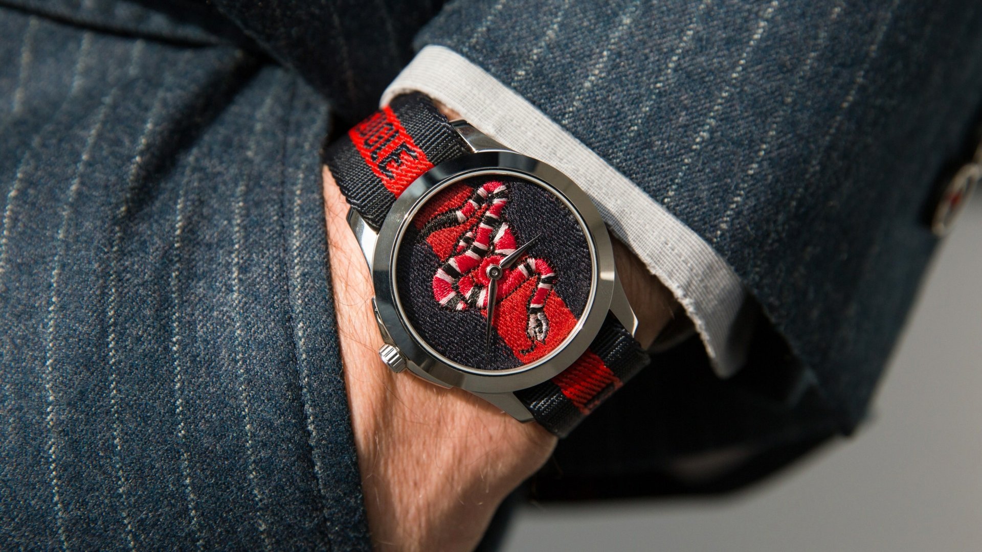 HD wallpaper featuring a Gucci watch with a red and black design on the wrist of a person wearing denim.