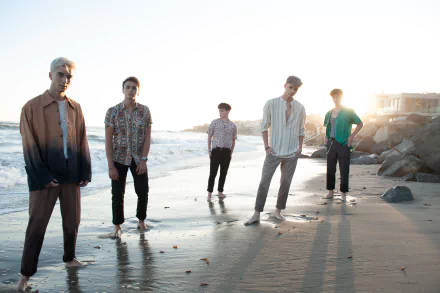HD desktop wallpaper of the band Why Don't We, standing together on a beach with the sun setting in the background.