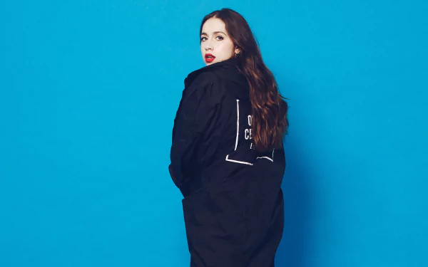 A person posing against a blue background in a black outfit, serving as a Tate McRae themed HD desktop wallpaper.