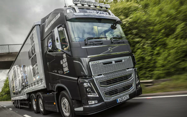 A striking HD desktop wallpaper featuring a Volvo FH16 750 truck in motion, showcasing its powerful design against a lush green backdrop.