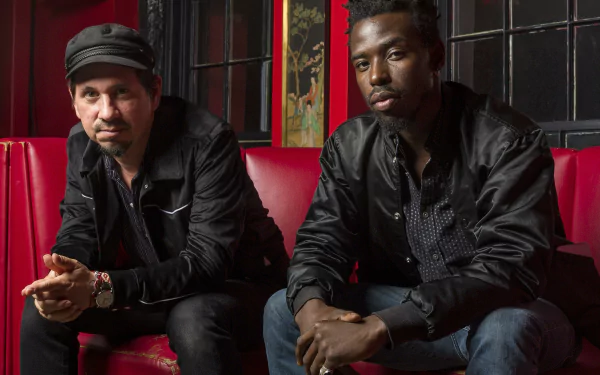 Two members of the music duo Black Pumas seated on a red couch, forming a stylish HD desktop wallpaper.