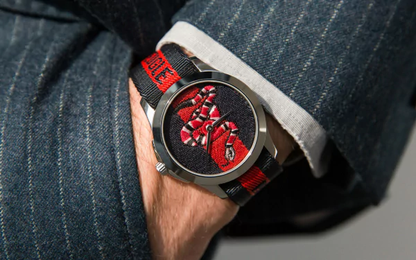 HD wallpaper featuring a Gucci watch with a red and black design on the wrist of a person wearing denim.