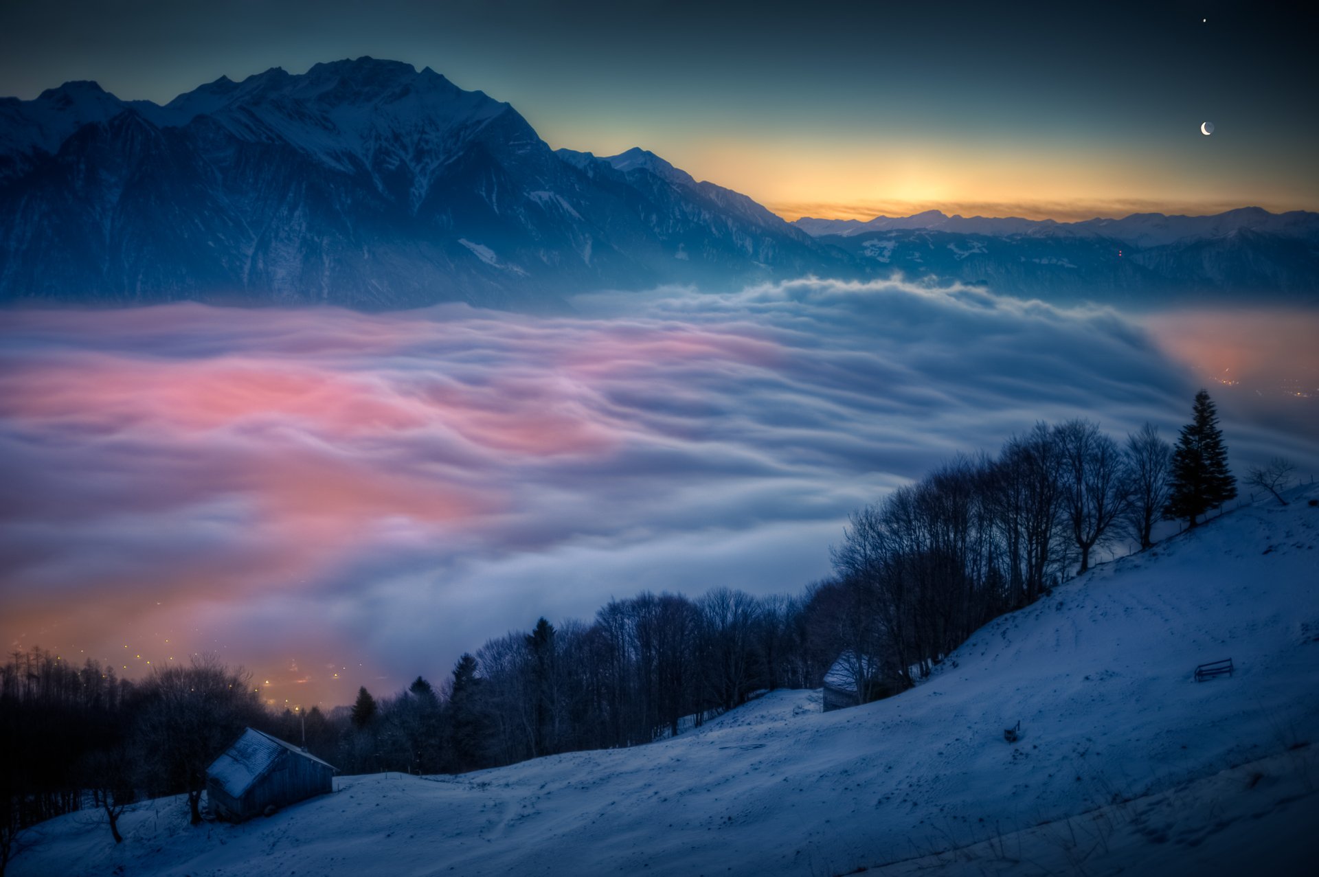 HD desktop wallpaper featuring a breathtaking winter evening landscape with a sea of clouds enveloping the mountain, creating a stunning contrast against the snow-covered slopes and twilight sky.