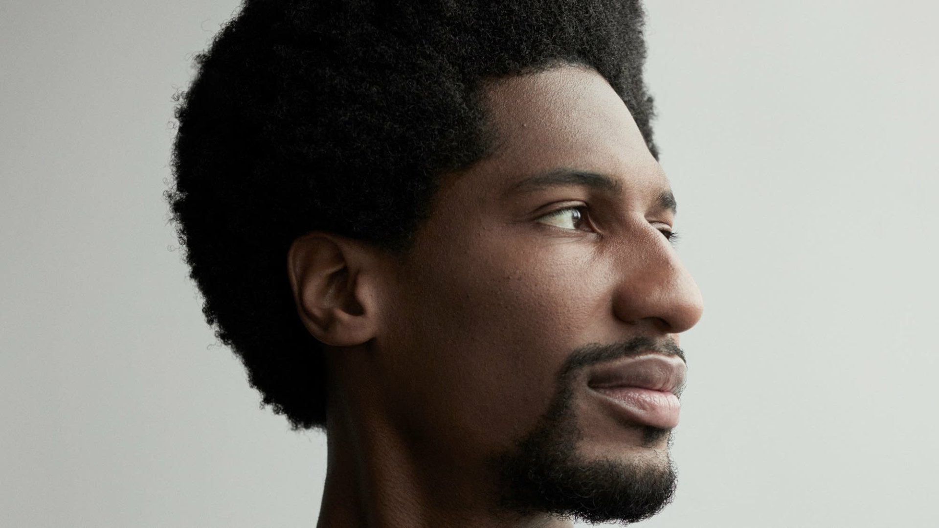 HD desktop wallpaper featuring a side portrait of a man with an afro against a neutral background.