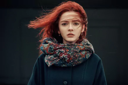 Redhead woman model wearing a patterned scarf and dark coat, hair blown by wind against a moody backdrop — 4K Ultra HD PC desktop wallpaper/background.