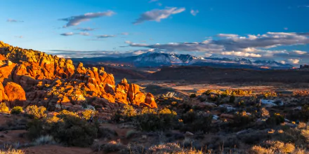5K Ultra HD PC desktop wallpaper: Utah, USA landscape with sunlit red rock formations in foreground and snow-capped mountains under a blue sky - vibrant mountain nature scene.