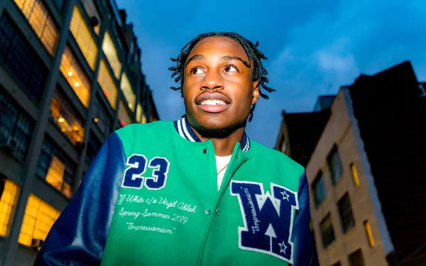 HD desktop wallpaper featuring a man in a green '23' varsity jacket set against a cityscape during dusk.