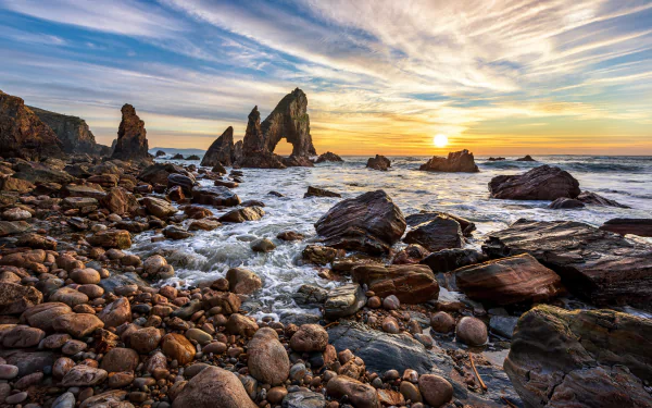 4K Ultra HD wallpaper of Ireland’s rocky coast at sunrise, featuring a natural arch, ocean waves, and a vibrant sky over the horizon in a stunning seascape.