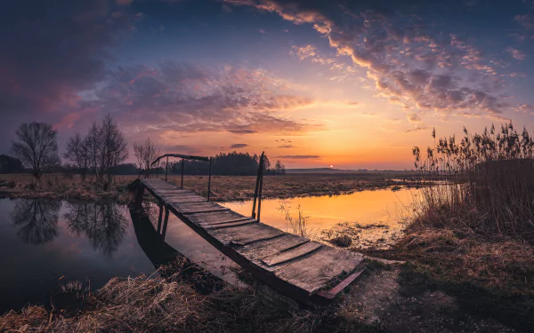 HD outdoor desktop wallpaper featuring a serene body of water at sunset with a rustic man-made wooden bridge extending into the scene.